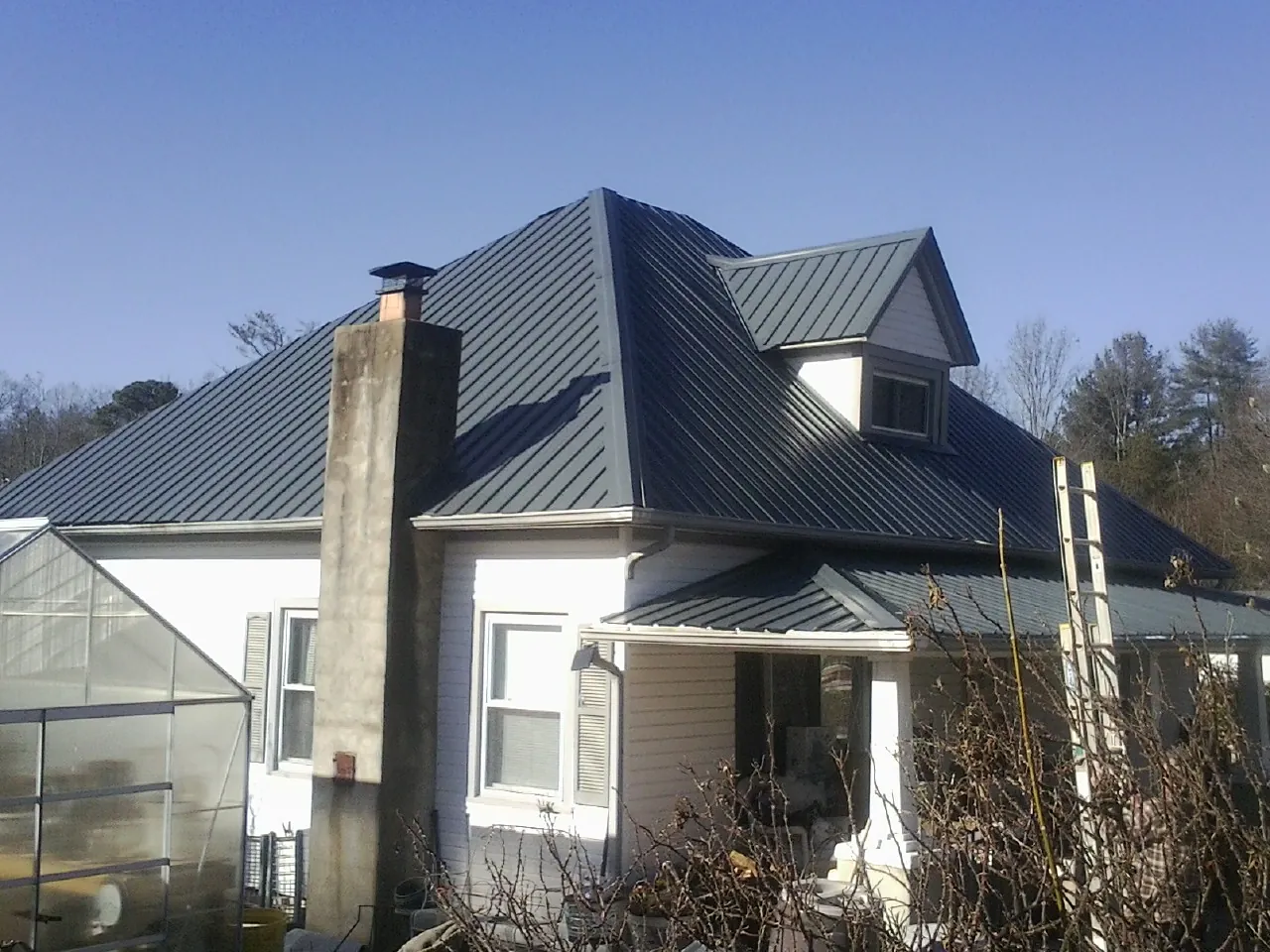 Dark blue standing seam metal roof on a white farmhouse with dormer — Slate & Tile Roof Repair by Roofing Brothers in Parkton