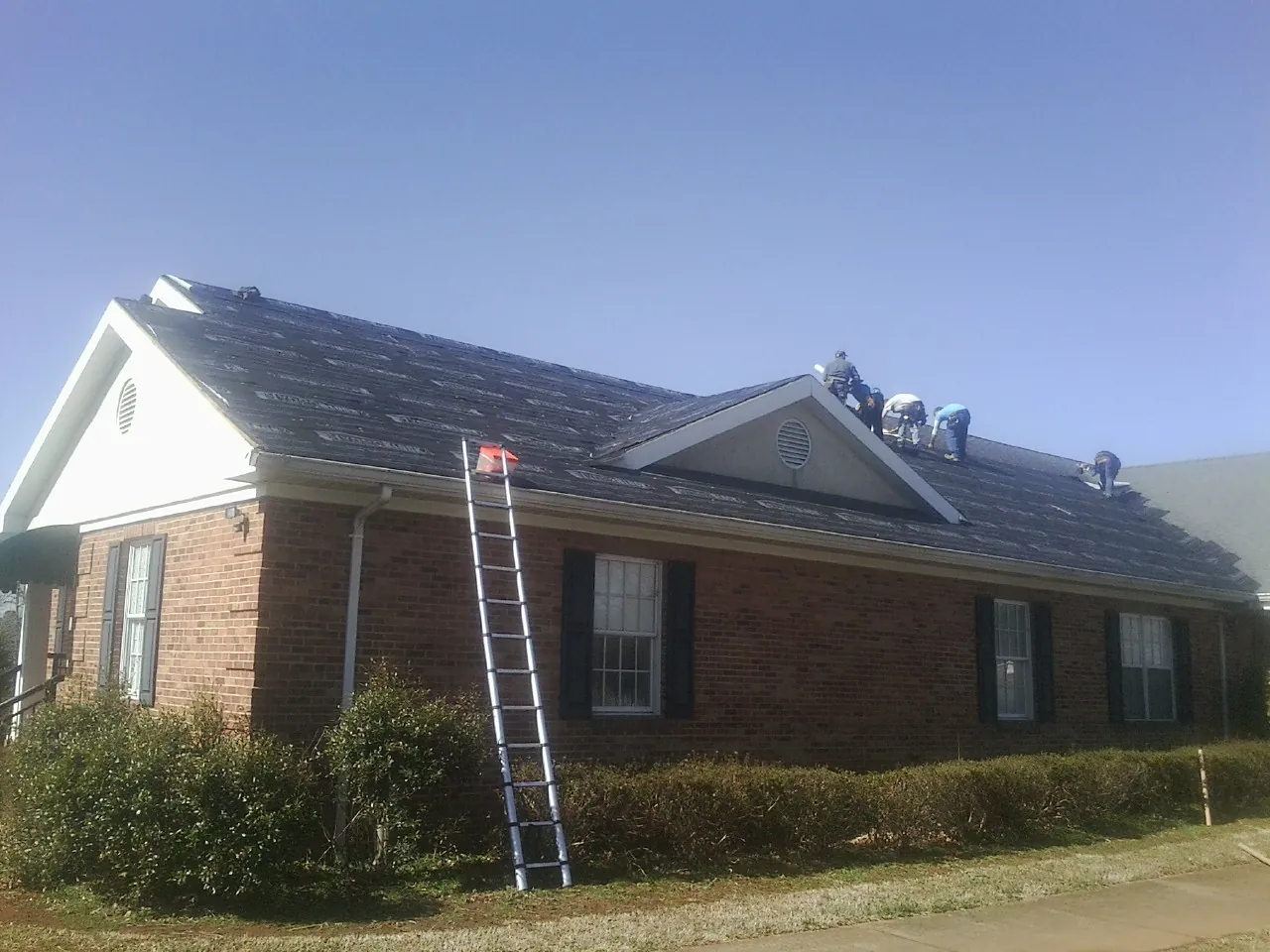 Crew tearing shingles off a brick ranch roof with a ladder set — Metal Roof Repair work by our crew in Parkton
