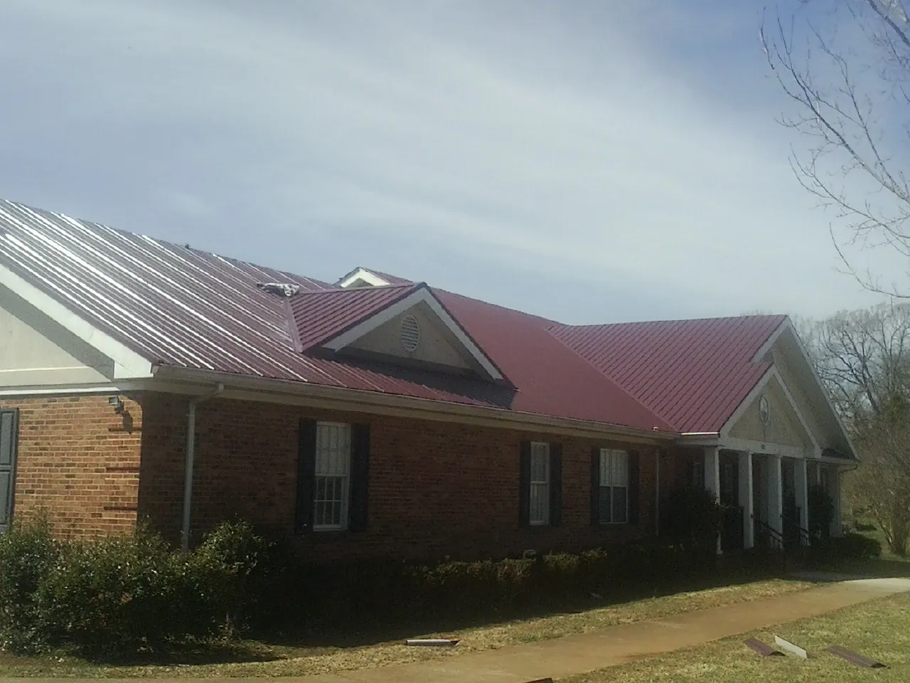 Red metal roof with gabled entries on a long brick building, from a Hail Damage Roof Repair job in Parkton