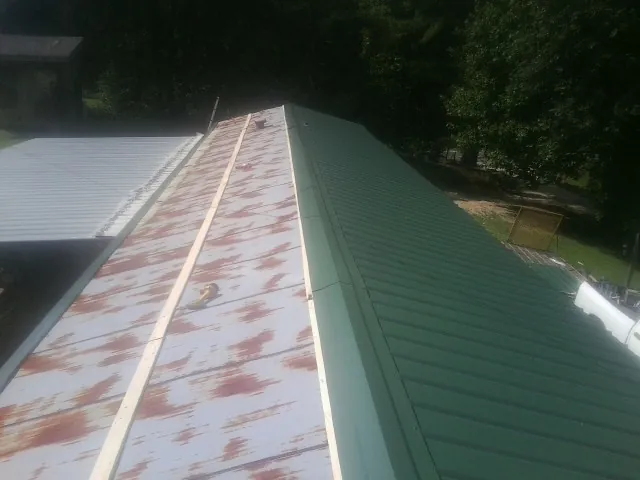 Old rusted panels beside newly installed green metal roofing — Wind Damage Roof Repair by Roofing Brothers in Parkton