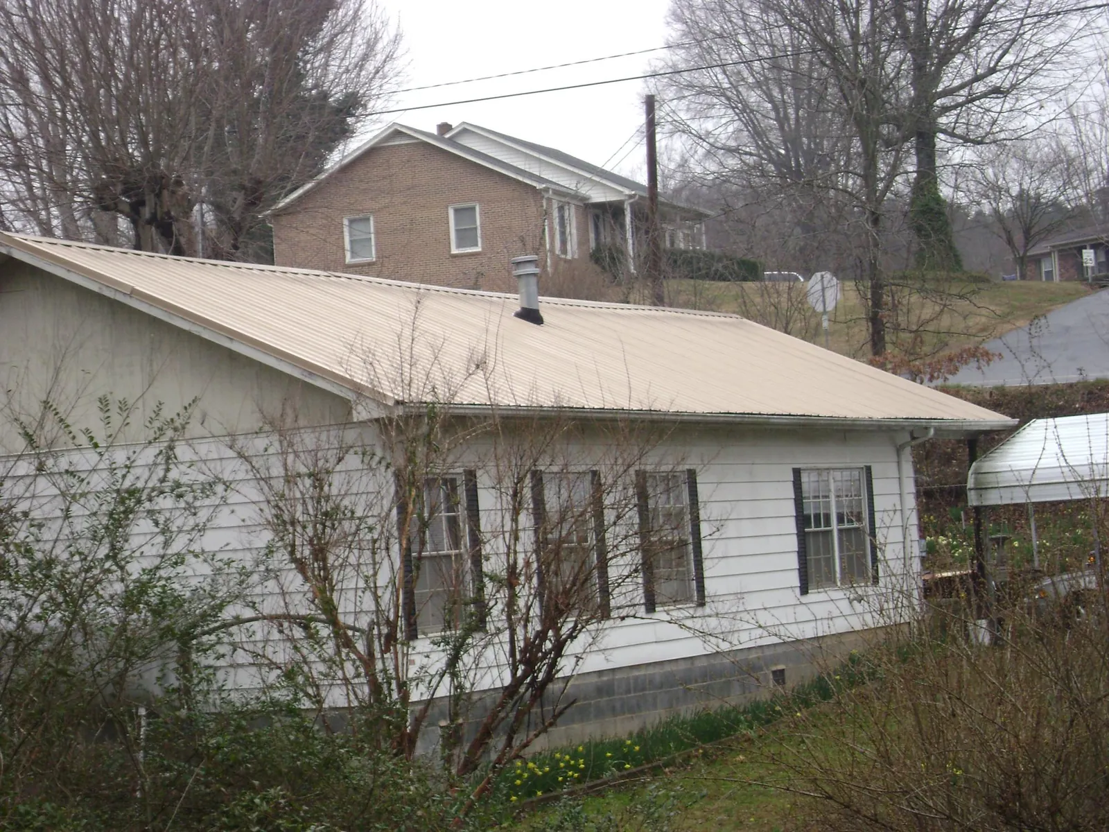 Tan metal roof on a white sided house set into a hillside — Commercial Roofing by Roofing Brothers in Parkton