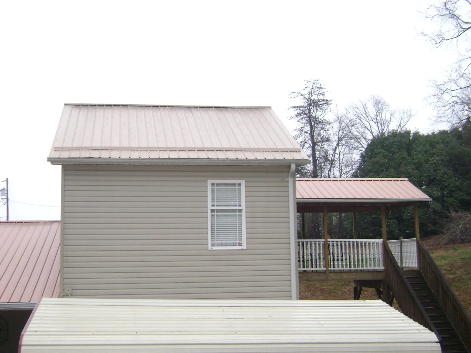 Tan metal roofs on a two story addition and attached porch, from a Roof Replacement job in Parkton
